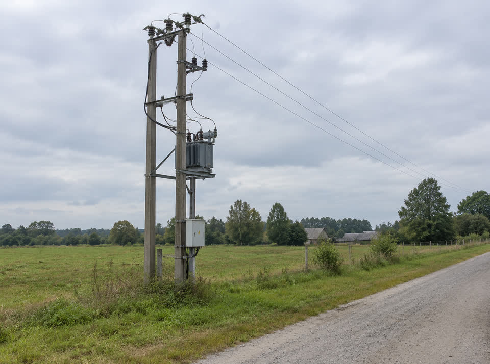 Mała stacja transformatorowa na słupie przy żwirowej drodze i łące